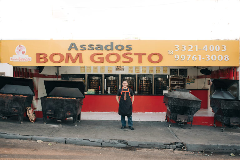 Fachada da loja Assados Bom Gosto com João Marcelo na calçada