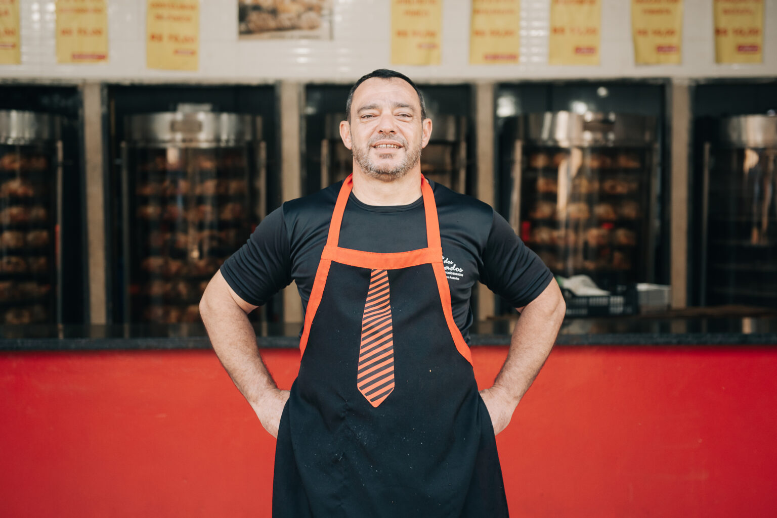 João Marcelo Gonçalves entre as máquinas de frango assado da loja Assados Bom Gosto